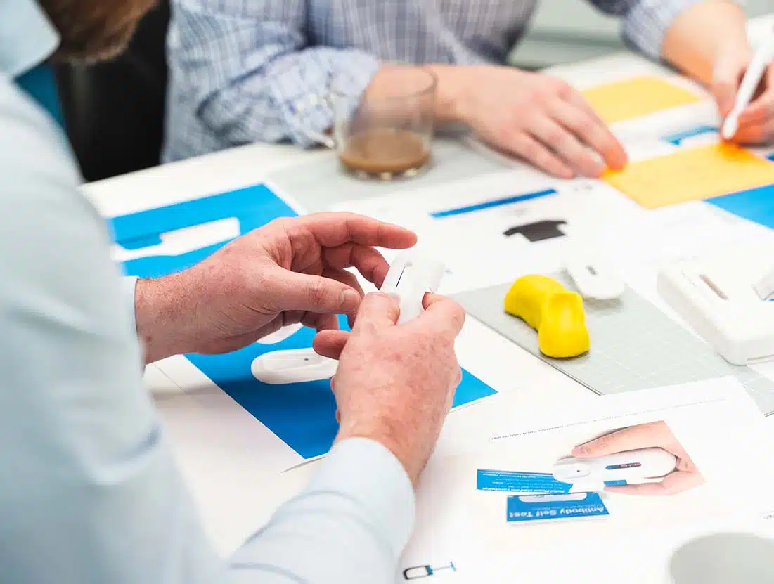 Two designers discussing 3D prints and sketching concepts for a blood sampling diagnostics device in a medical device design development services meeting